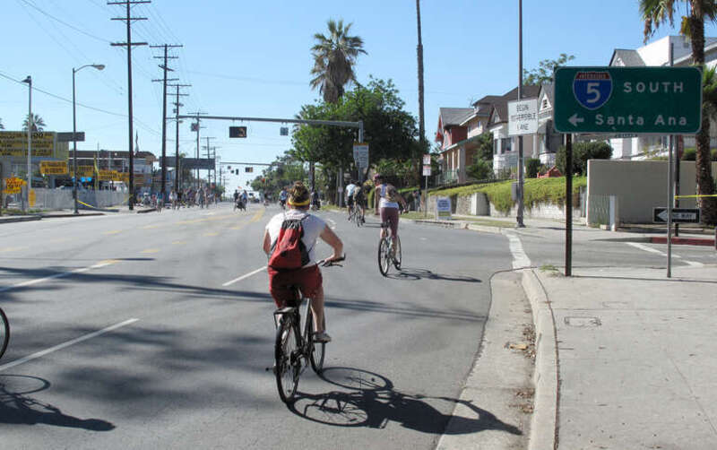 CicLAvia 2010 bicyclists heading west on Fourth Street, passing an exit ramp from Interstate 5 that has been closed with yellow tape. An entrance ramp to Interstate 5 southbound is just to the left of the image.