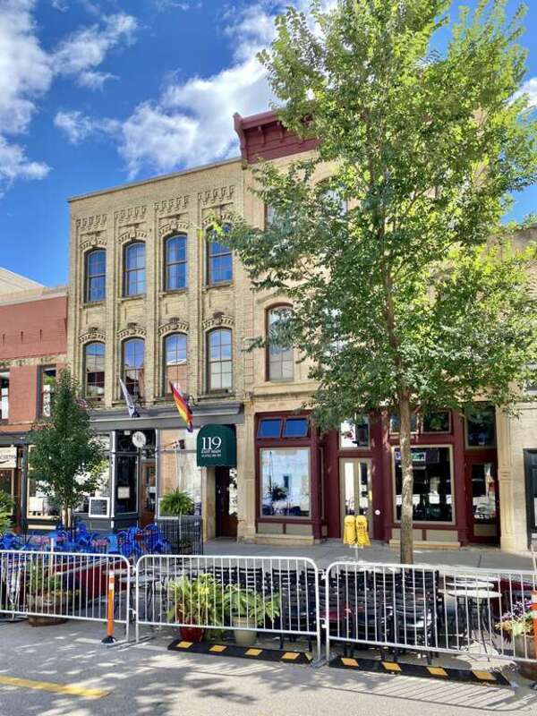 On the left, built in 1868, this Italianate-style building is known as Thompson’s Block, and features a buff brick exterior with limestone pilasters flanking the storefronts on the first floor, which feature cast iron columns, arched four-over-four
