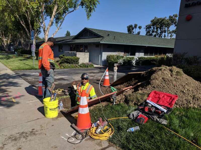 Two men at work, one standing in an excavated trench next to the sidewalk along Hamilton Avenue in Campbell, California.