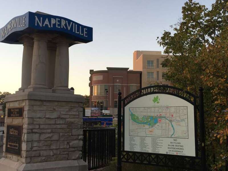Early morning photograph with a subtle sunrise, taken at the Naperville Riverwalk park on the west branch of the DuPage river. The view is facing Water Street and Downtown Naperville. There is some renovation activity in the background during the