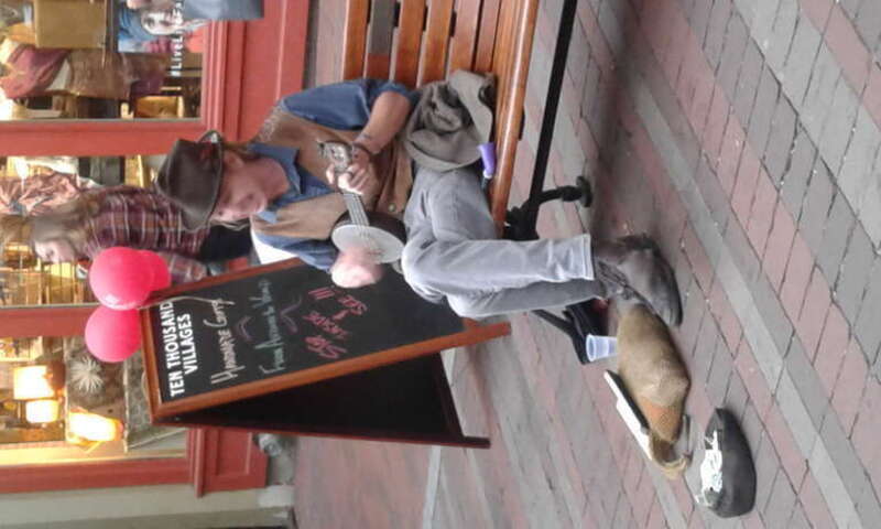 Street performer playing small banjo and singing on bench along downtown pedestrian mall in Burlington, Vermont.
