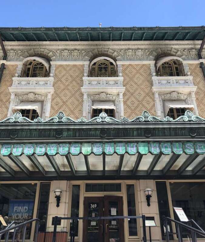 Large 3 story building with ornately carved windows and a large green porch with a stained glass panels that spell out "Fordyce Bath House."
The front of the Fordyce Bathhouse. The building was originally built in 1915 and today serves as the Park's