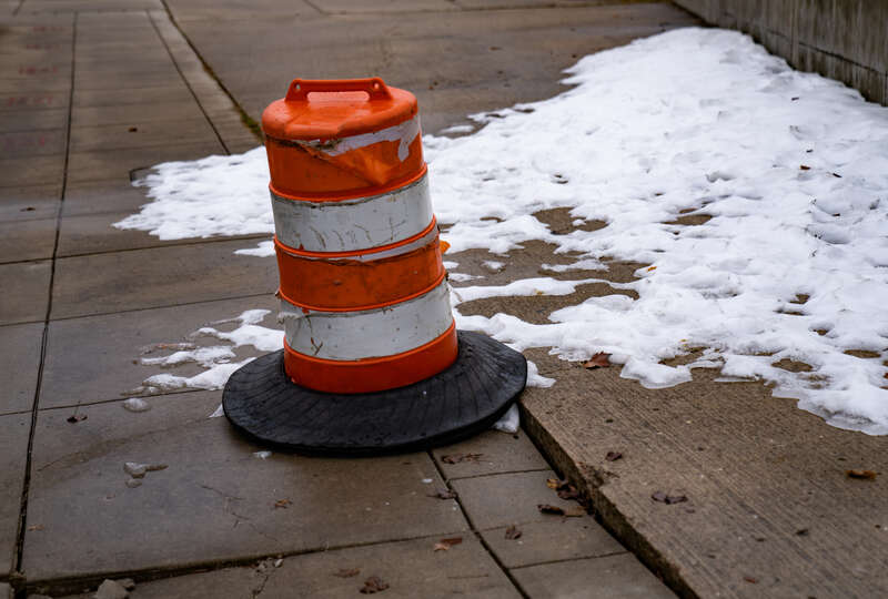 A traffic cone warns of uneven sidewalk pavement, which is also snow and ice-covered, in Traverse City, Michigan.