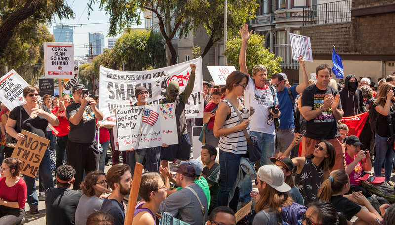 Protesters sit and stand in the street, holding various signs and banners, at a Patriot Prayer counter-protest in San Francisco.