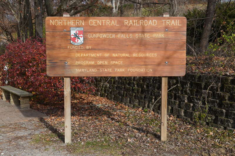 A wooden sign that reads:
NORTHERN CENTRAL RAILROAD TRAIL
GUNPOWDER FALLS STATE PARK
FUNDED BY
DEPARTMENT OF NATURAL RESOURCES
PROGRAM OPEN SPACE

MARYLAND STATE PARK FOUNDATION