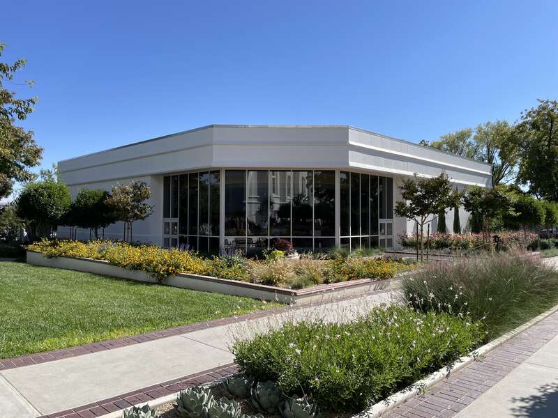 The St. George Temple visitors center, a concrete path leads to the building, along a path of grass, bushes and shrubbery.