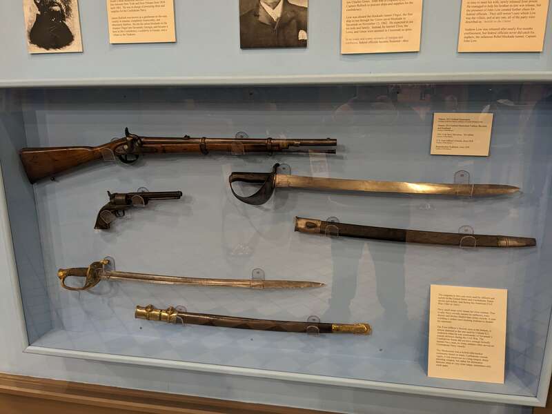 Display of swords and firearms belonging to the Union and Confederate Navies during the US Civil War, including an 1853 Enfield Musketoon, an 1853 Enfield Cutlass Bayonet and Scabbard, an 1851 Colt Navy Revolver, and a US Foot Officer's Sword with a