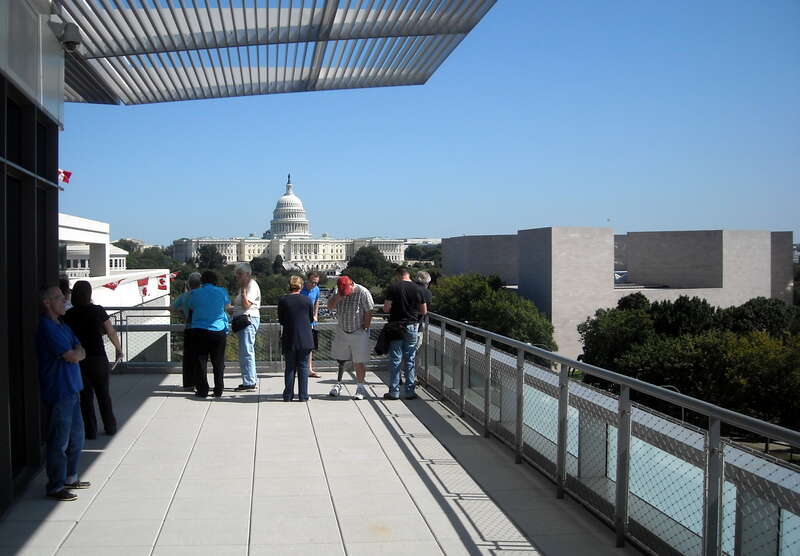 People standing on the Newseum's Hank Greenspun Terrace, which overlooks Pennsylvania Avenue and the National Mall in Washington, D.C.  The United States Capitol, the East Building of the National Gallery of Art, and the Embassy of Canada are visible