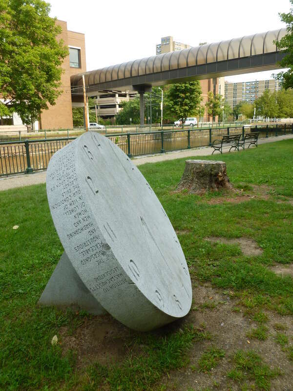 The left side of a 14 hour clock monument at Lucy Larcom Park, made by Ellen Rothenberg in 1996.  The work memorializes the &quot;10 hour movement&quot; of the early 1800's, spearheaded by female workers in Lowell.  
An inscription that circles along the