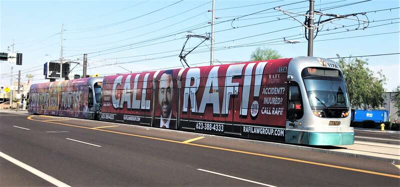 A Valley Metro Rail Train on East Washington Street between North 54th Place and North 48th Street, across from Tovrea Castle. The train is wrapped in advertising.