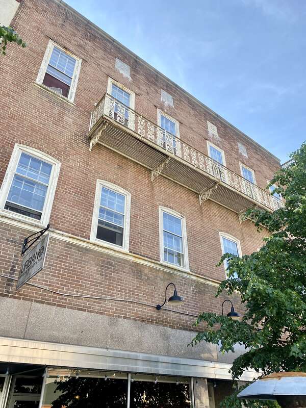 Built in the 19th Century, this building features a red brick exterior, nine-overnice and six-over-six double-hung windows, arches above the second floor windows, a cast iron balcony in the center of the front facade on the third floor, two first