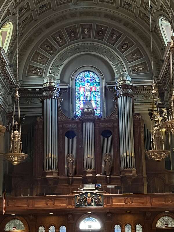 Interior view of the Cathedral Basilica of Saints Peter and Paul in Philadelphia, PA, showing an organ on a balcony and some stained glass windows, walls, lamps, etc.