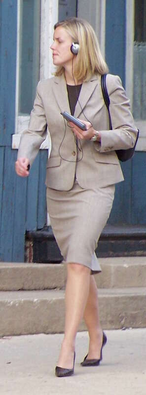 A woman listening to a Walkman audio device while walking on a city street.