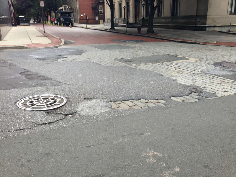 The intersection of Barack Street and West Front Street in Trenton, New Jersey, with asphalt potholes revealing a sett surface beneath