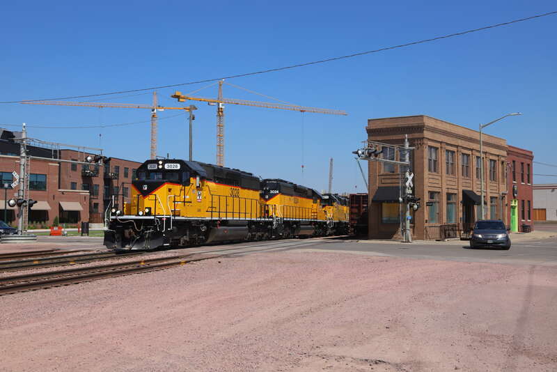 After waiting for traffic to clear on the Canton Sub, D&amp;amp;I loads get underway in downtown Sioux Falls. Ahead is the grade south of town where the train stalled and had to shove back past here to 60th Street N to meet helpers coming down from Dell.
