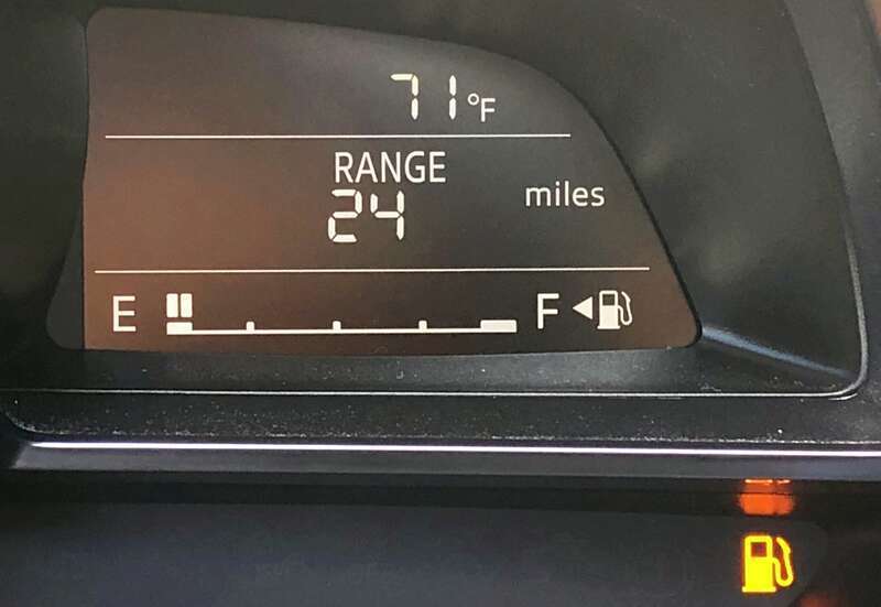 The digital fuel gauge on a 2018 Mazda 3, showing a nearly-empty tank with the low fuel level warning light illuminated.