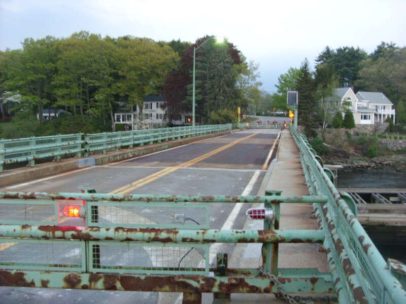 The old Hines Bridge, built in 1966 and known as the Essex–Merrimack Drawbridge until about 2006, with its gates/barricades pivoted out across the roadway to stop traffic just before an opening of the swing span for river traffic. This bridge closed