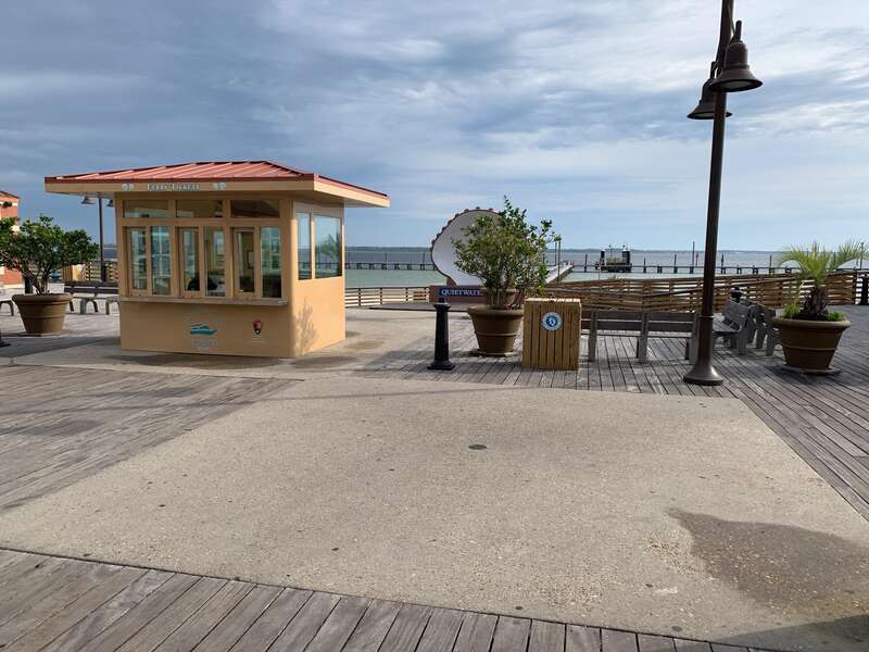 Small yellow building and wooden benches on a wooden and cement boardwalk. Pensacola Bay in the background.
Tour Boat Pier Pensacola Beach