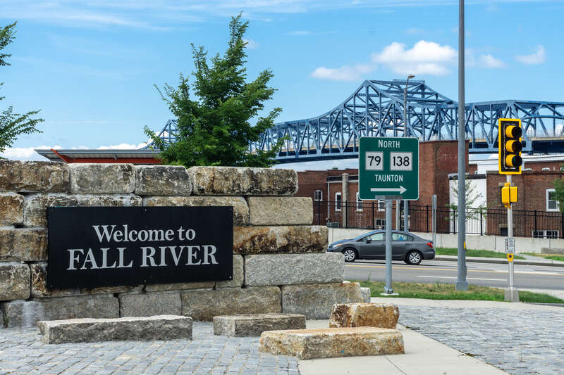 Sign says &quot;Welcome to Fall River&quot; with the Braga Bridge behind it.