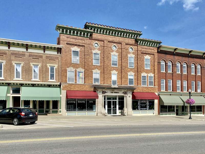 On the left, built in the late 19th Century, this Italianate-style building features a red brick facade with a bracketed cornice featuring modillions and dentils, stone lintels and sills, pilasters between the window bays with recessed brick panels