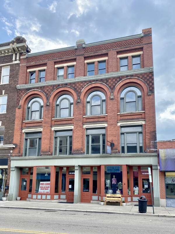 Built in 1895, this Romanesque Revival-style building features a red brick exterior, arched windows on the third floor, stone trim, decorative patterned brickwork, one-over-one double-hung windows, and a modified first floor retail shopfront.  The