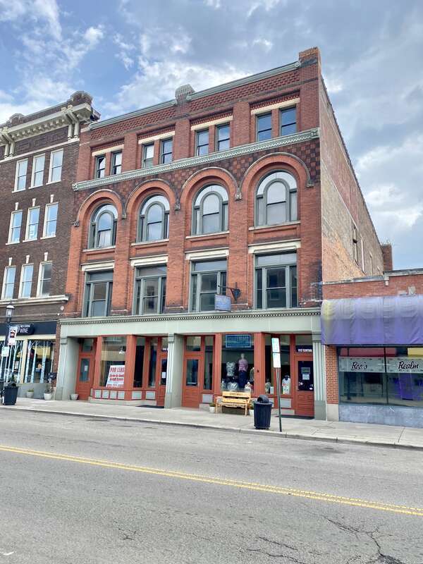 Built in 1895, this Romanesque Revival-style building features a red brick exterior, arched windows on the third floor, stone trim, decorative patterned brickwork, one-over-one double-hung windows, and a modified first floor retail shopfront.  The