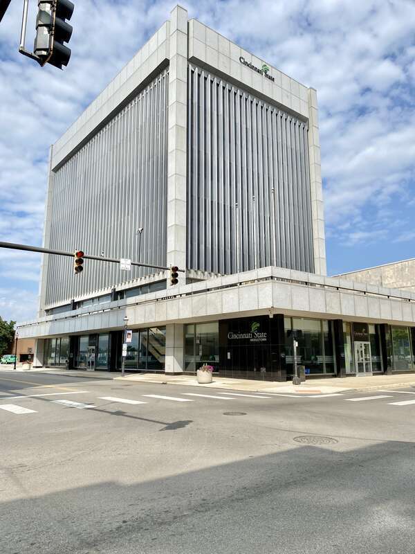 Built in 1969, this Modern International-style skyscraper features a stone panel and metal-clad exterior with a one-story podium featuring a large parapet and dark stone-clad columns, a plaza atop the roof of the podium with planters and flagpoles,