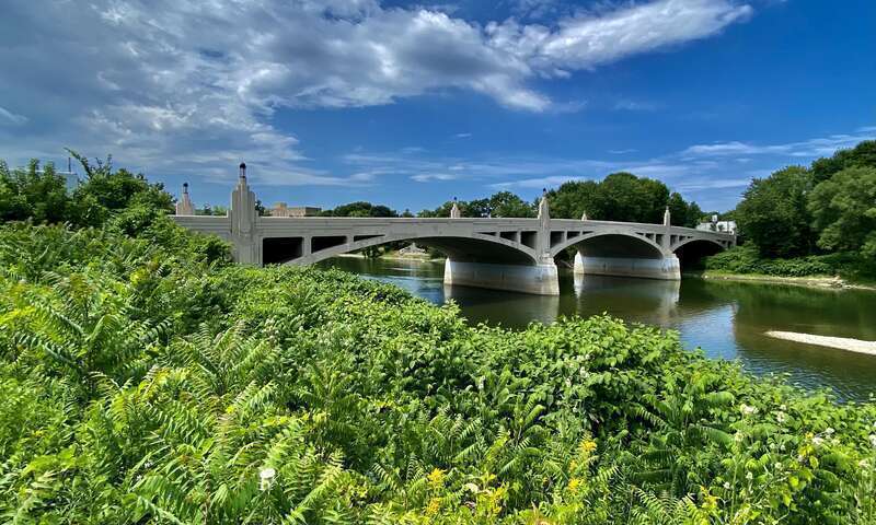 As seen in July 2022 from the back of the parking lot at the northwest corner of Water Street next to Ray's Auto Shop, this concrete open-spandrel deck arch bridge has carried traffic on East Clinton Street over the Chenango River and into downtown