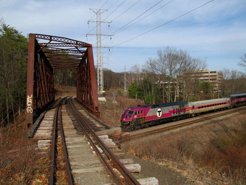 An outbound Fitchburg Line train passes under the former Central Massachusetts Branch bridge in Weston, Massachusetts in April 2017