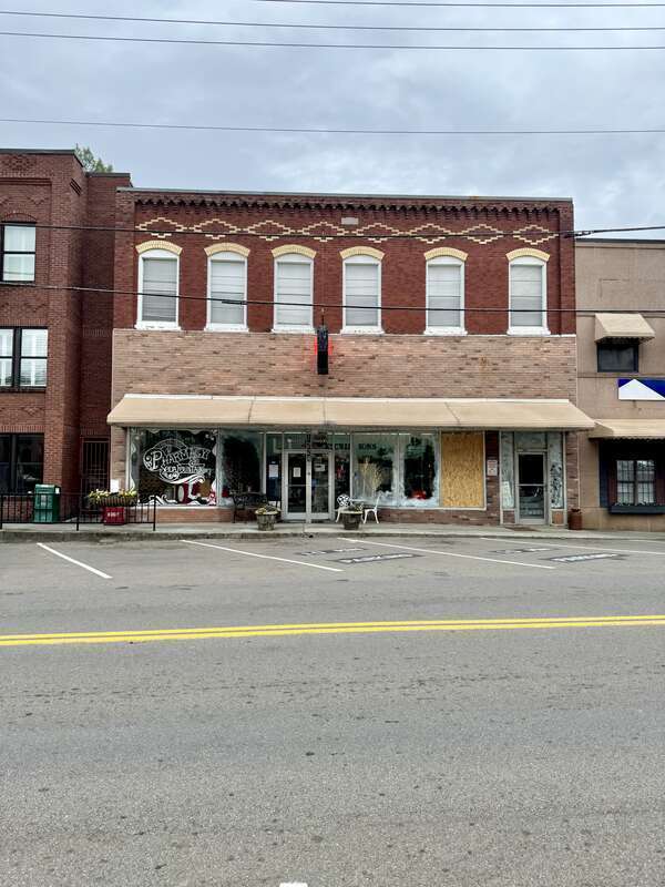 Built in 1919, this two-story commercial building features a red brick exterior, one-over-one windows in arched bays on the second floor, buff brick trim, a corbeled brick cornice, a pale pink brick first floor with a recessed entrance door flanked