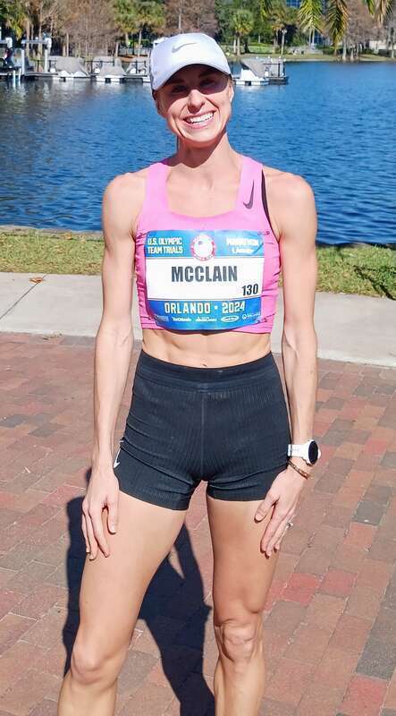 Athlete runner with a white hat, pink running top and black shorts.