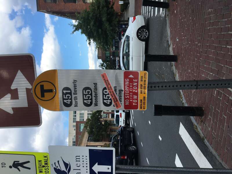 An MBTA bus stop sign for routes 451, 455, and 459 in downtown Salem in August 2019. Route 459 is crossed out by a sticker indicating the route's discontinuance two days later.