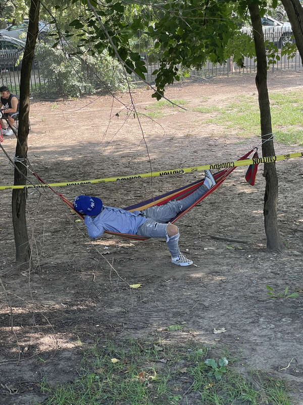 A man wearing a blue Yankee's hat chills in a hammock in Prospect Park, Brooklyn, NYC.