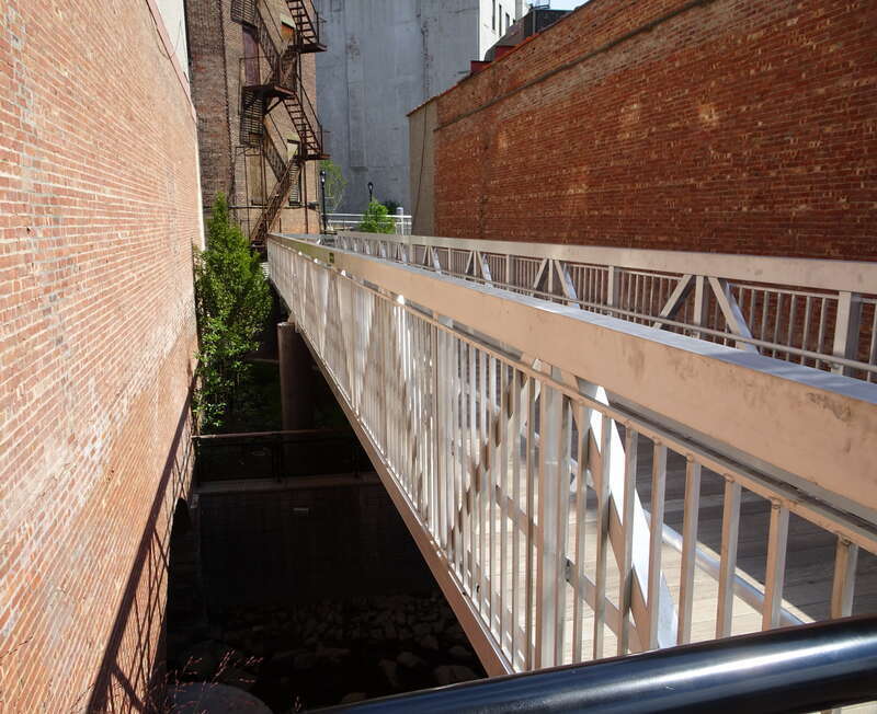 Looking southeast at bridge over creek in Mill Street Plaza Park on a sunny midday.