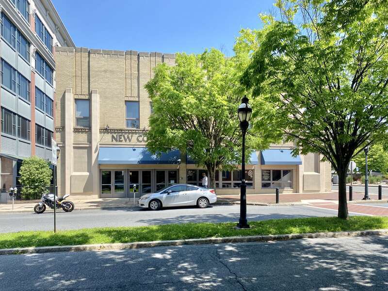 Built in the early 20th Century, this Art Deco-style building features a buff brick front facade and stucco-clad sides, stone trim, recessed panels above the window openings, decorative trim above the windows and below the parapet cap, decorative