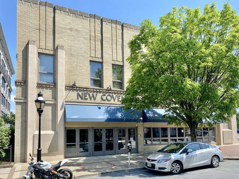 Built in the early 20th Century, this Art Deco-style building features a buff brick front facade and stucco-clad sides, stone trim, recessed panels above the window openings, decorative trim above the windows and below the parapet cap, decorative