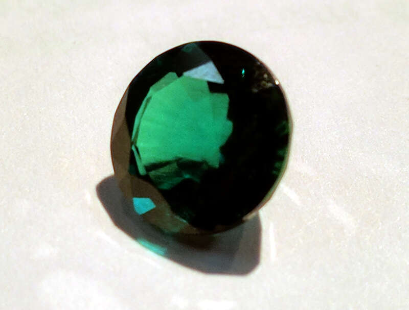 A 9mm round cut synthetic emerald, produced by the hydrothermal process.