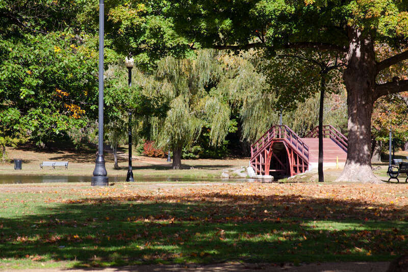 A view looking west in Worcester, Massachusetts' Elm Park with pond and footbridge visible.