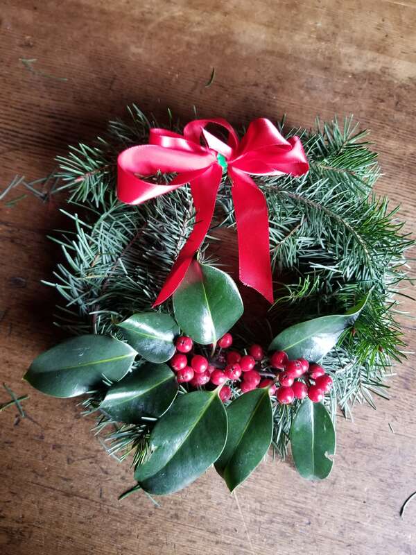 The holiday wreath with evergreen boughs, a sprig of holly, and a red satin ribbon tied on.
Tie a bow with the ribbon and attach it to the wreath using the thin wire.