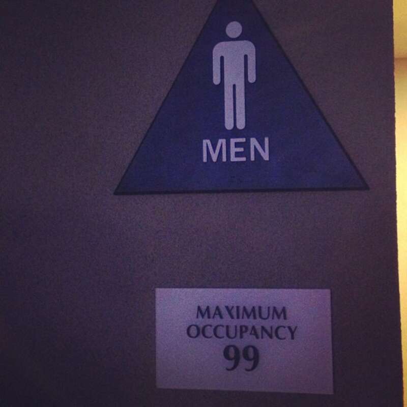 A sign stating the maximum occupancy of a men's restroom.