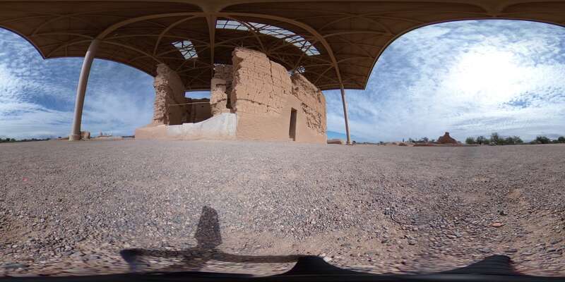 Spherical image of the ruins of a two-story Adobe structure, which has a door and a collapsed corner. There is a prominent metal overhang covering the runs.
Drag your cursor or use the controls at the bottom of the image to navigate this 360-degree