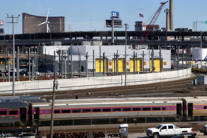 The new Green Line Extension Vehicle Maintenance Facility and surrounding areas viewed from a northbound train on Red Bridge in March 2022. Commuter rail trains at the Commuter Rail Maintenance Facility are in the foreground; in the background are