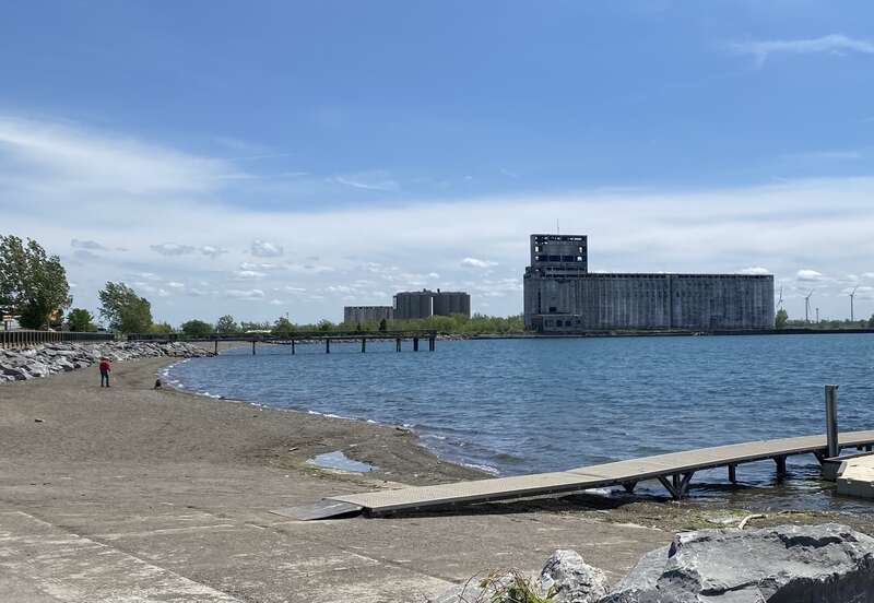 With the Cargill Pool Elevator as a lofty backdrop, a man plays fetch with his dog at Gallagher Beach in Buffalo Harbor State Park in Buffalo, New York, on a bright and sunny May 2021 afternoon.