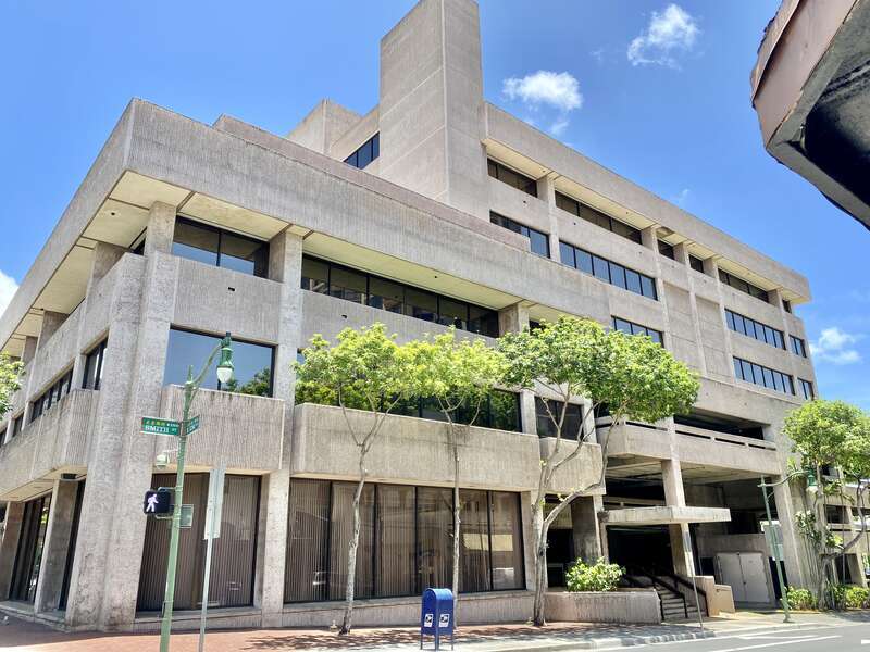 Built in 1960, this Brutalist building was constructed as the headquarters of the Hawaii National Bank.  The building features a rough textured concrete exterior, boxy geometric forms, a protruding parapet on the exterior facing walls, ribbon