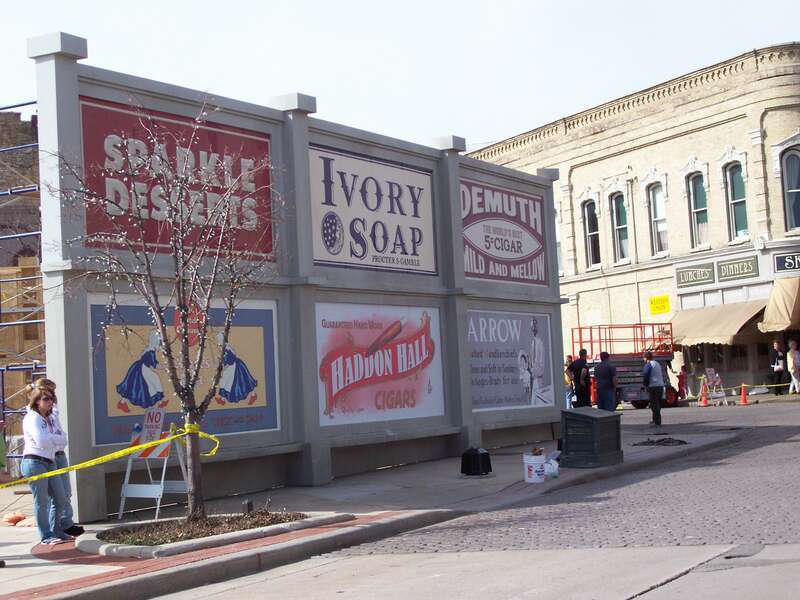 Fake advertisement signs to hide a sundial and some modern benches.