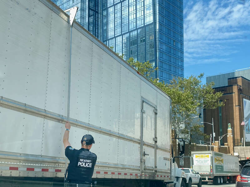 Police officer uses overheight stick to measure the truck's height at the west bound entrance of Lincoln Tunnel after the red light is trigger by this truck.