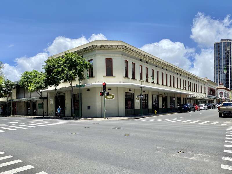 Built in the early 20th Century, this Classical Revival-style commercial building, featuring a stucco clad-exterior, bracketed cornice, and arched one-over-one double-hung windows, is a contributing structure in the Chinatown Historic District,