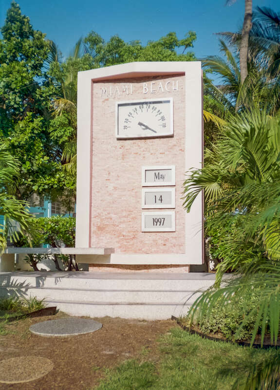 Tropical sun beating down on the landmark Art Deco temperature gauge surrounded by palm trees in Lummus Park, South Beach, Miami's first public park (Ocean Drive, Lummus Park, South Beach, Miami, Florida, USA)