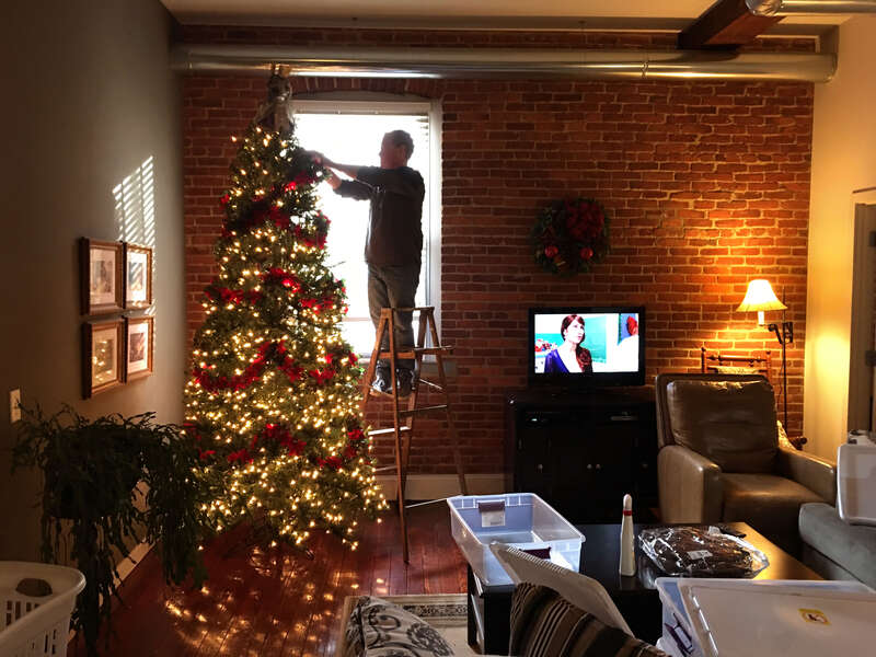 Man on ladder decorating Christmas tree in living room