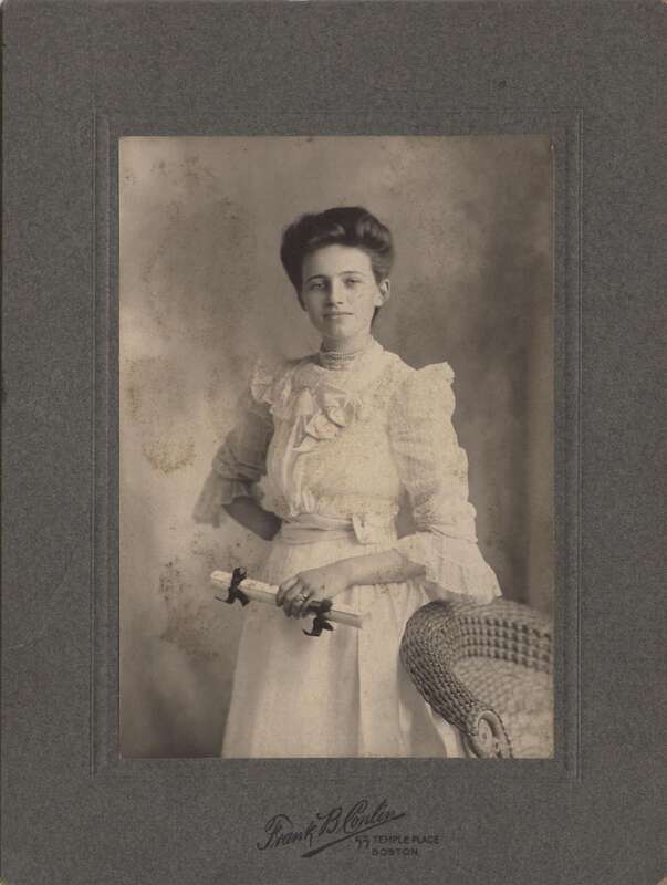 New Graduate? Or Newly married? Not sure. She's holding a scroll that could be a diploma but she is also wearing a nice wedding set on her left ring finger. I Think at the time of the photo wedding dresses mostly did not come in white and in fact